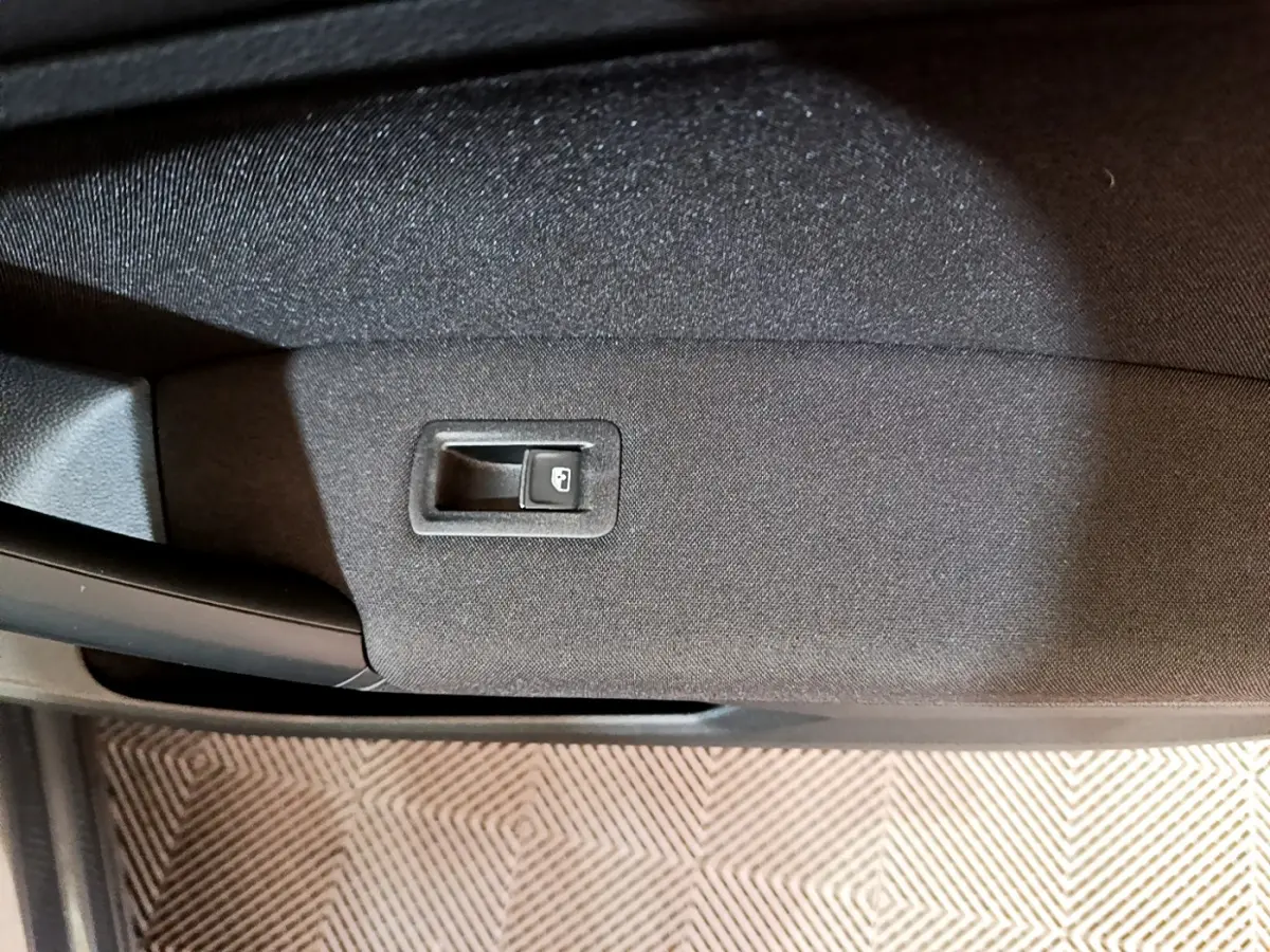 Gros plan sur le bouton d'ouverture de coffre intégré à la garniture intérieure d'une Volkswagen Tiguan gris clair.