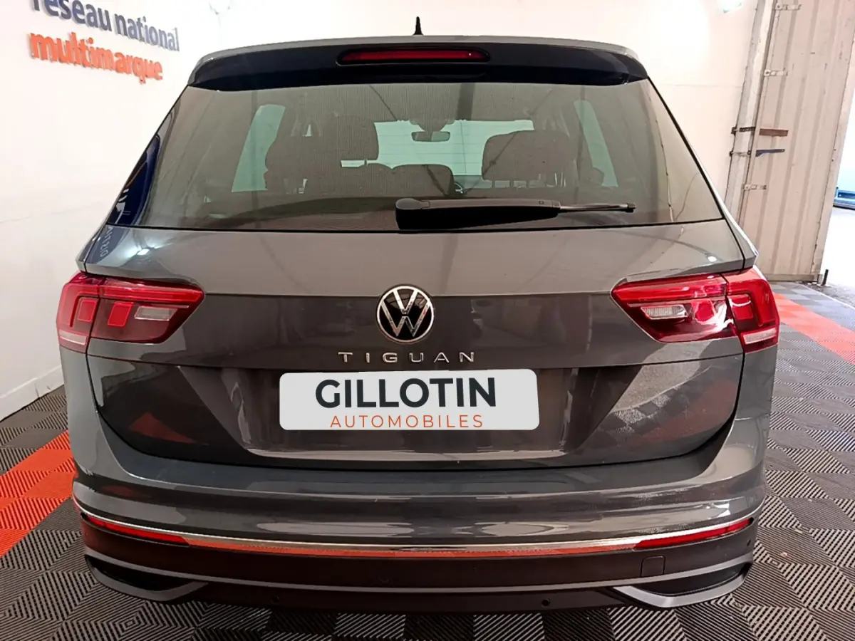 Vue arrière d'un Volkswagen Tiguan gris clair 2021 avec feux LED et logo VW bien visibles, en intérieur showroom.