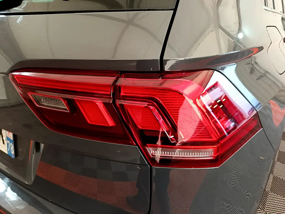 Gros plan sur le feu arrière droit rouge d'un Volkswagen Tiguan gris clair 2021, avec reflet sur la carrosserie lisse.