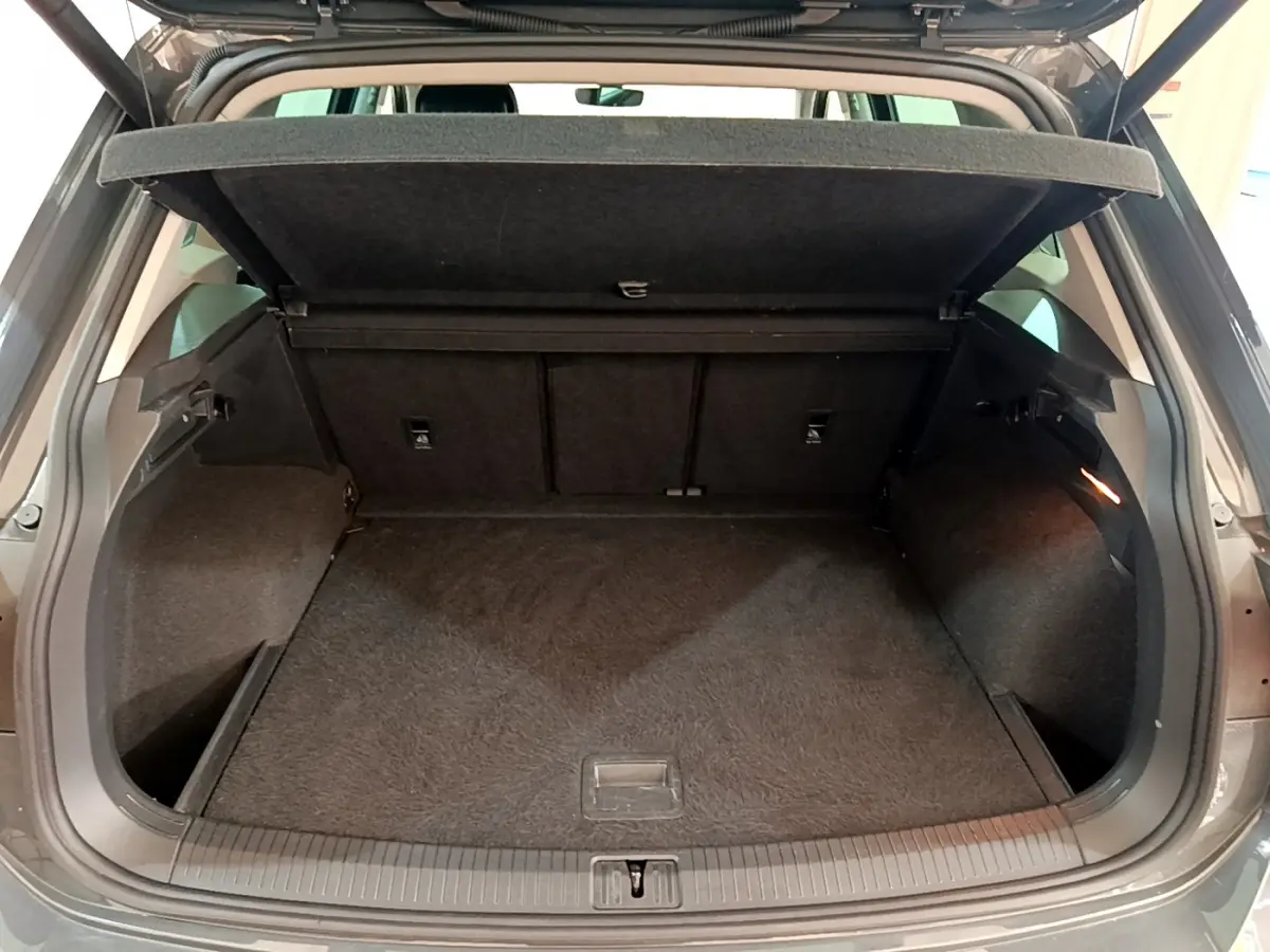 Coffre ouvert vu de l'arrière d'un Volkswagen Tiguan gris clair, espace de chargement vide et tapis noir.