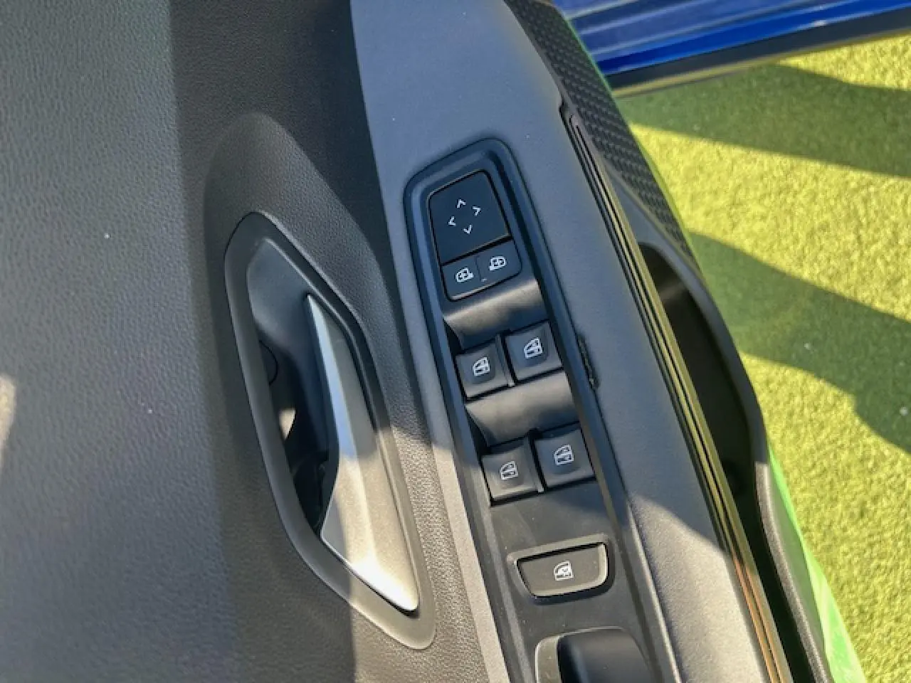 Détail des commandes de lève-vitres et rétroviseurs sur la porte côté gauche d’une Dacia Sandero III Stepway bleu Iron.