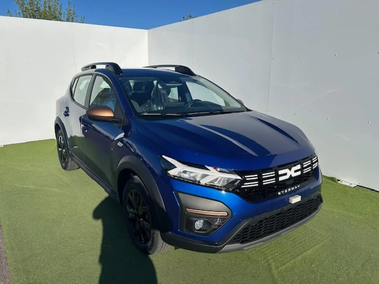 Dacia Sandero III Stepway bleu Iron vue 3/4 avant droit avec calandre noire et barres de toit noires.