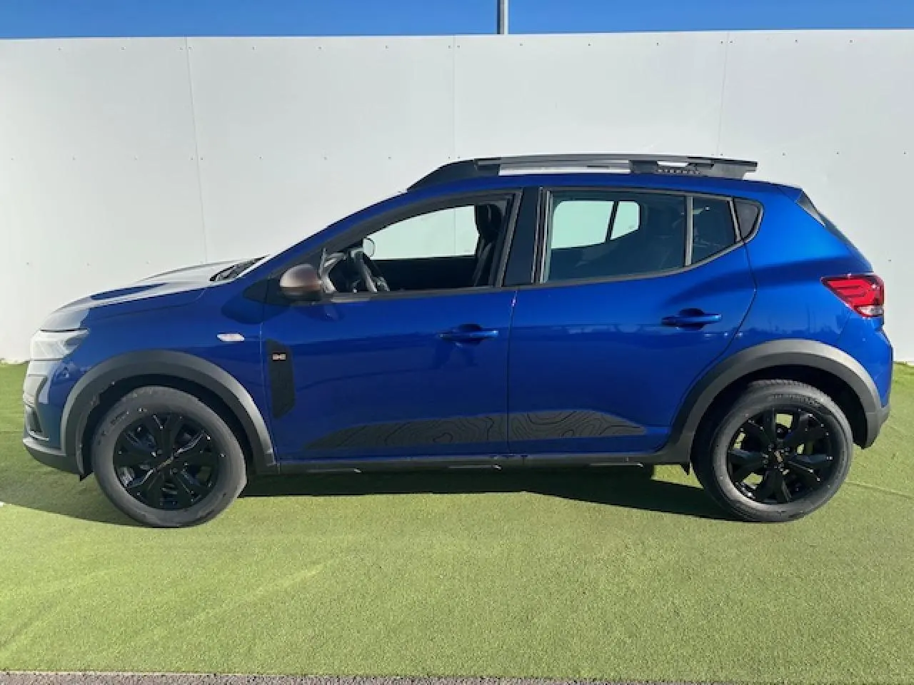 Profil droit d'une Dacia Sandero III Stepway bleu Iron avec jantes noires et barres de toit gris Mégalithe.