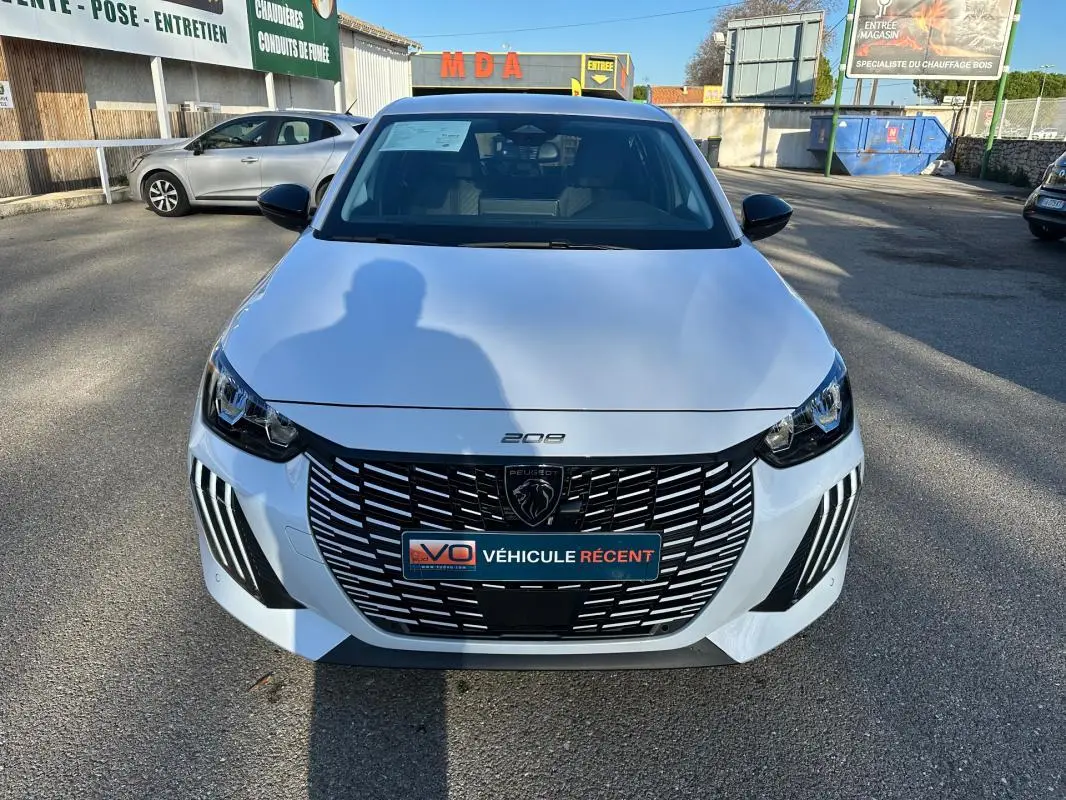 Vue avant d'une Peugeot 208 Hybrid 110 e-DCS6 Allure blanche, avec calandre noire et phares LED distinctifs.