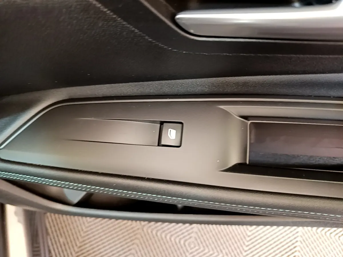 Gros plan sur la commande de lève-vitre côté conducteur, avec surpiqûres bleues sur le panneau de porte noir.