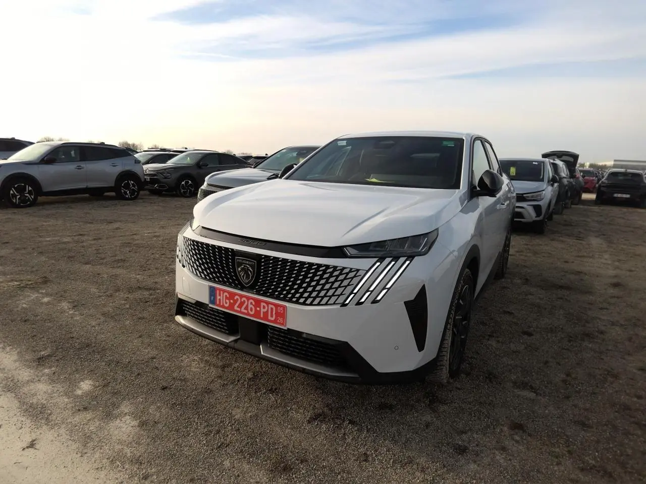 Peugeot 3008 blanc vue 3/4 avant avec calandre à motif géométrique et feux LED griffés, sur parking extérieur.