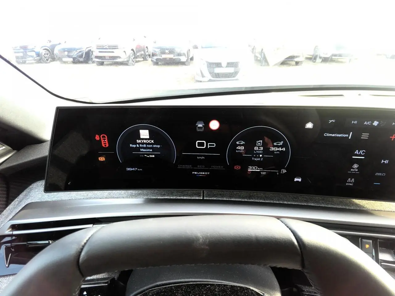 Vue intérieure du tableau de bord numérique du Peugeot 3008 hybride 2025 avec affichage multifonction et volant partiel.