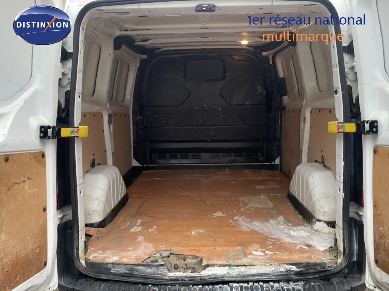 Vue arrière intérieure du fourgon Ford Transit Custom blanc, montrant l'espace de chargement avec plancher en bois usé.