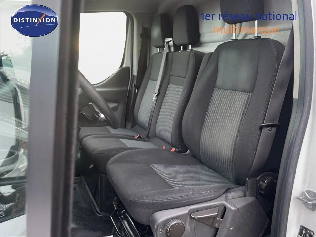 Vue intérieure côté conducteur du Ford Transit Custom blanc 2016, montrant les sièges tissu noir à trois places.