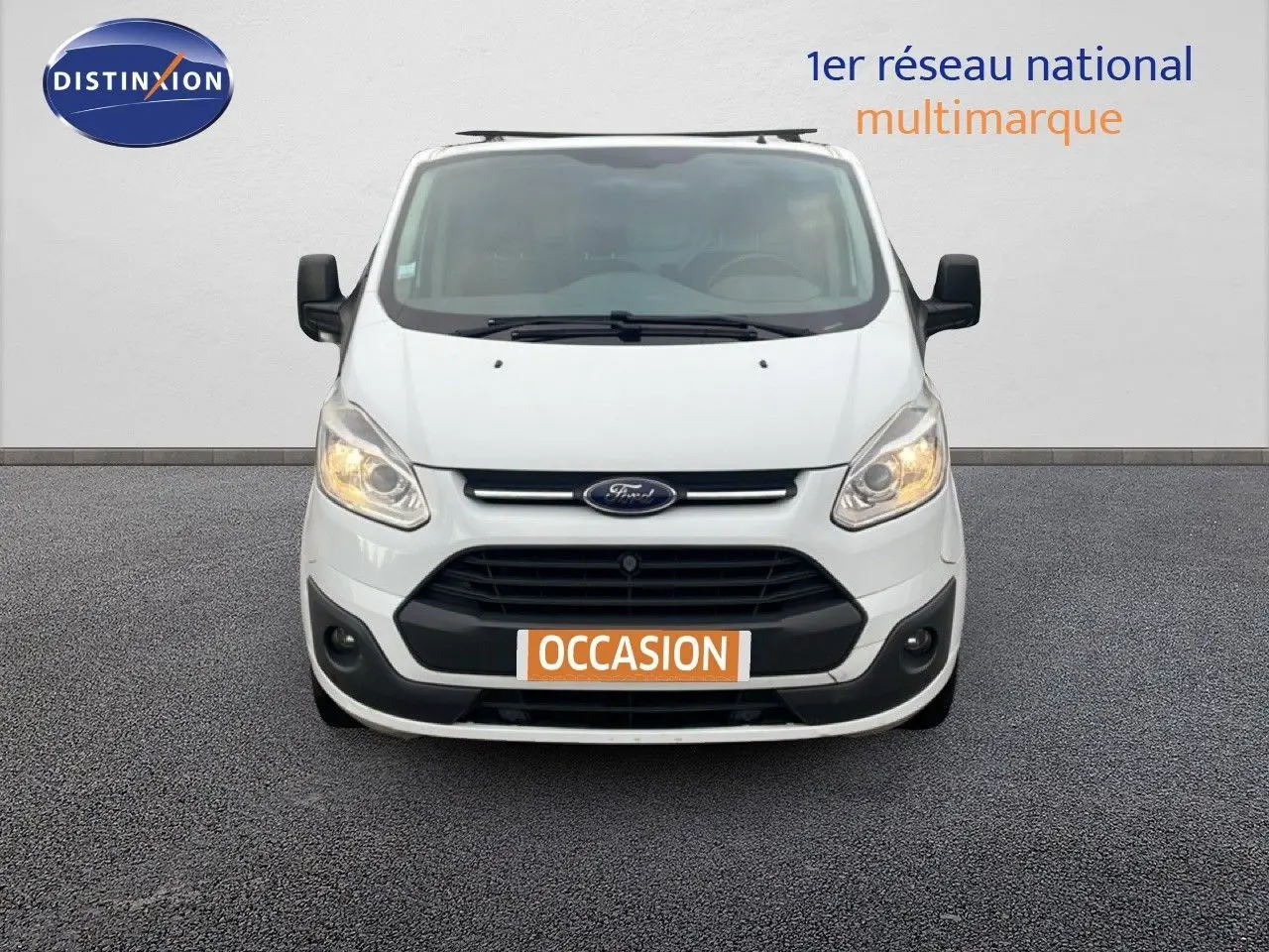 Vue frontale d'un Ford Transit Custom blanc de 2016 avec plaque "OCCASION" et phares allumés.
