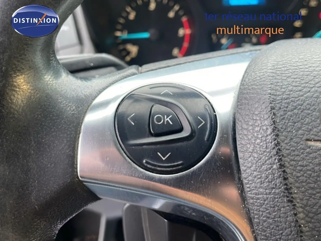 Gros plan sur les commandes au volant noir et argent du Ford Transit Custom blanc, modèle 2016, avec tableau de bord flou en arrière-plan.