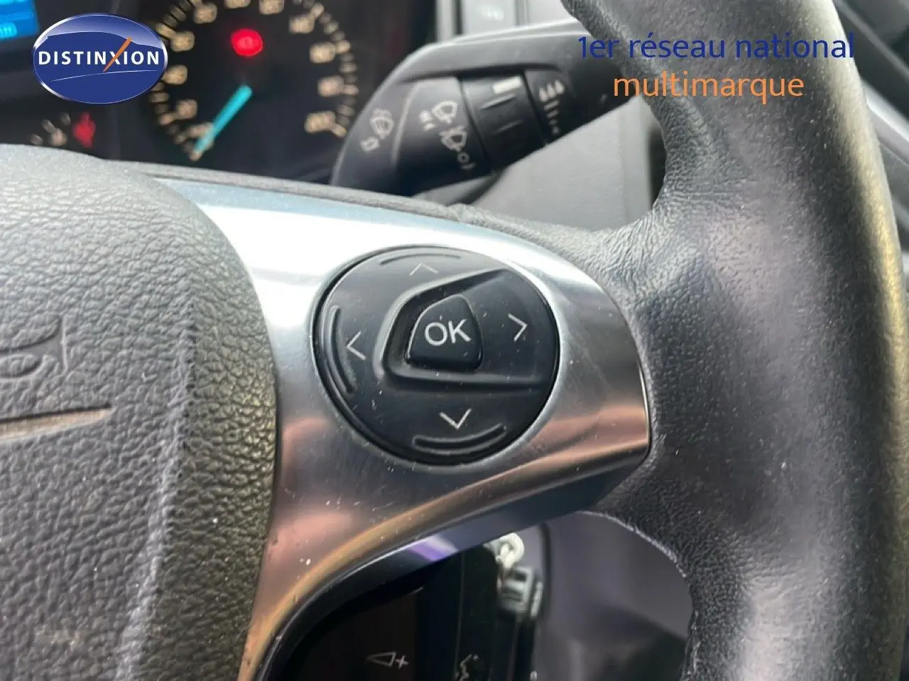 Gros plan sur le volant en cuir noir du Ford Transit Custom blanc, avec commandes multifonctions et tableau de bord en arrière-plan.