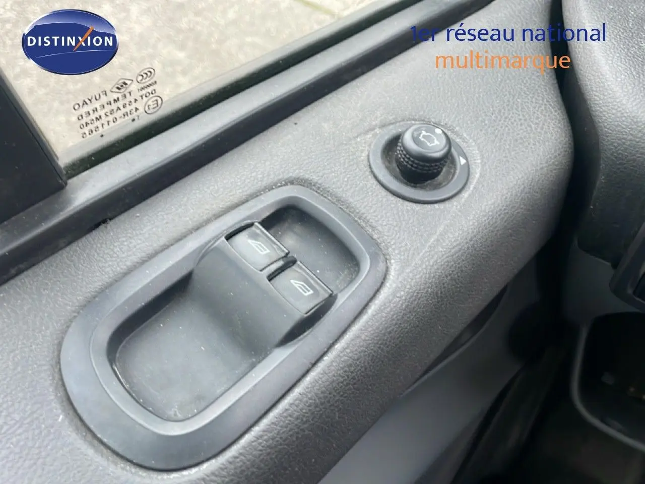 Gros plan sur les commandes de lève-vitres et réglage des rétroviseurs côté gauche d'un Ford Transit Custom blanc.