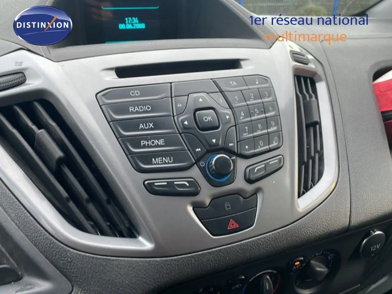 Vue rapprochée de la console centrale grise du Ford Transit Custom blanc, avec commandes radio et climatisation visibles.