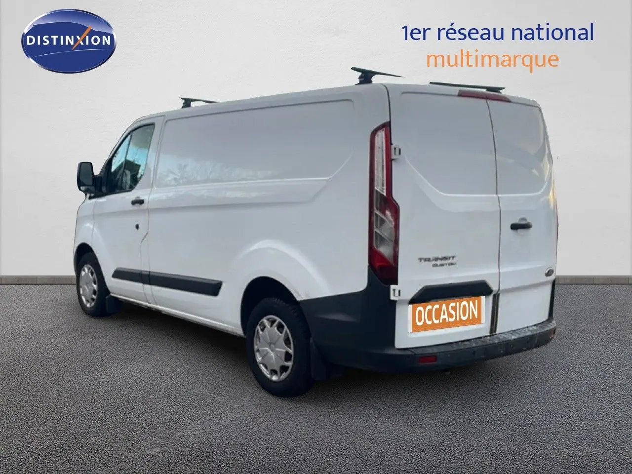 Ford Transit Custom blanc vu en 3/4 arrière côté gauche avec porte arrière et plaque occasion visible.