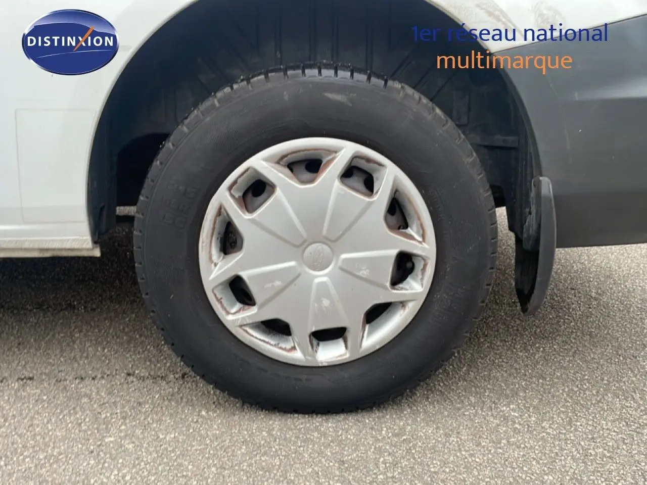 Gros plan sur la roue avant droite d'un Ford Transit Custom blanc de 2016 avec enjoliveur gris usé.