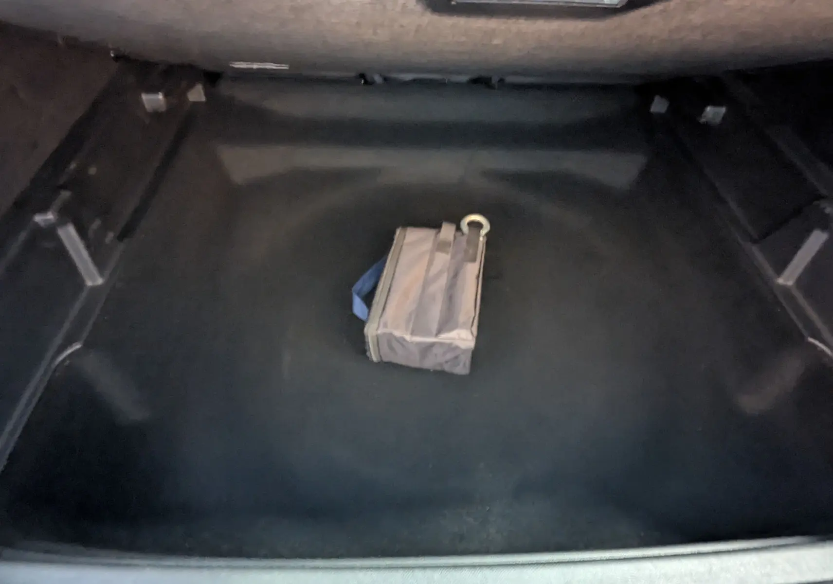 Vue du coffre ouvert du Peugeot 3008 Hybrid blanc 2025, avec un sac gris posé au centre sur le tapis noir.
