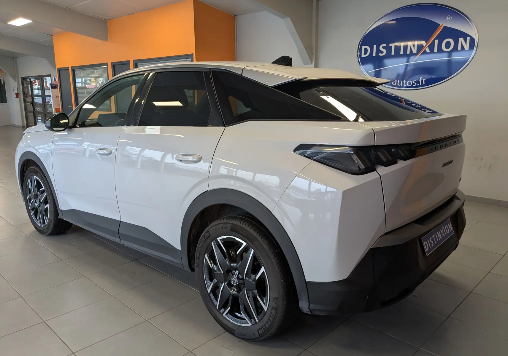 Vue 3/4 arrière droite d’un Peugeot 3008 Hybrid blanc avec jantes aluminium 19’’ et vitres arrière surteintées en showroom.