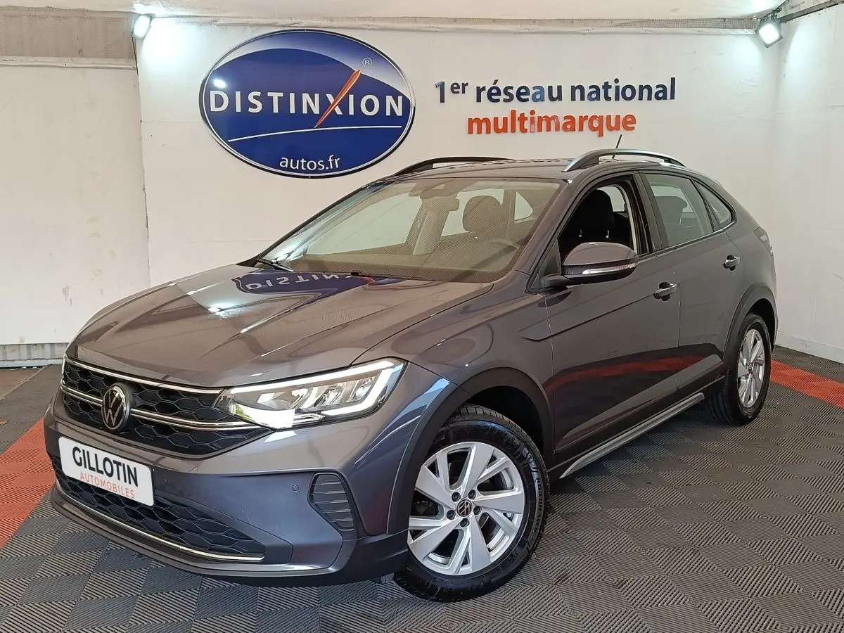 Volkswagen Taigo gris foncé en 3/4 avant droit dans un showroom avec logo Distinxion en arrière-plan.