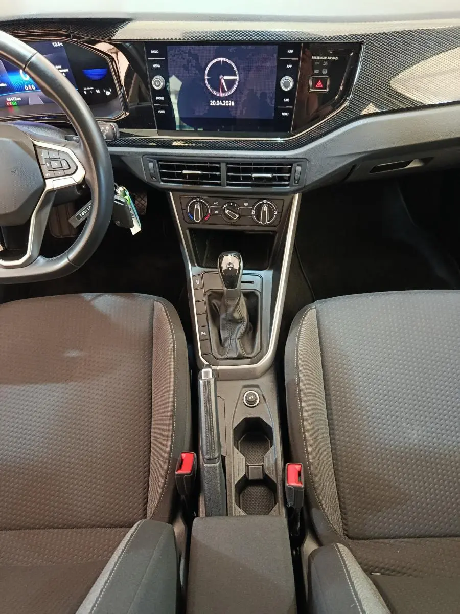 Vue intérieure centrée sur la console centrale et tableau de bord du Volkswagen Taigo gris foncé avec écran tactile et levier de boîte auto.