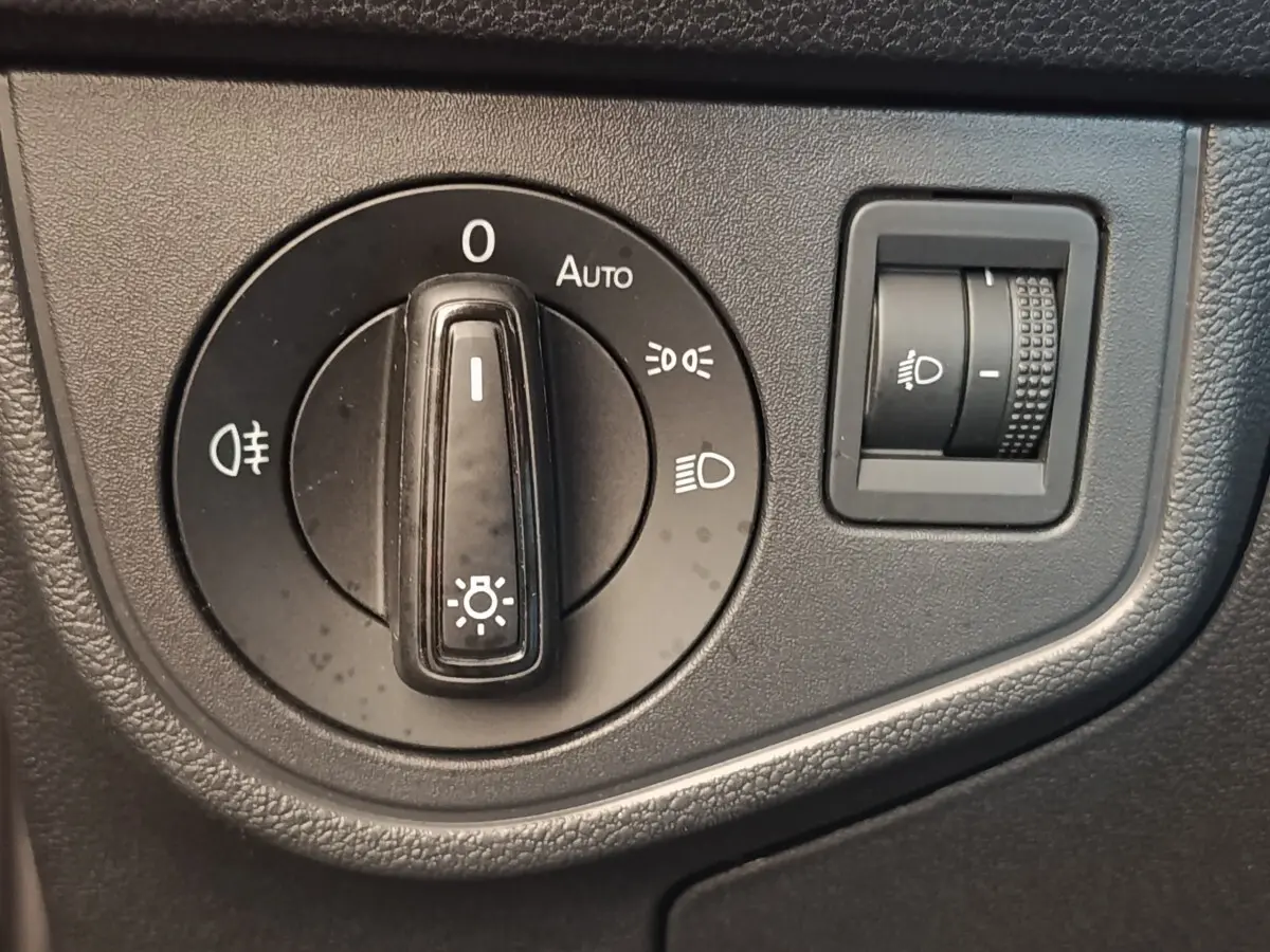 Gros plan sur la molette de réglage des phares et le bouton de réglage en hauteur dans un Volkswagen Taigo gris foncé.