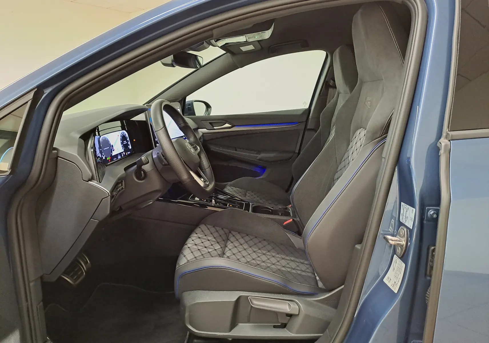 Vue intérieure côté conducteur de la Volkswagen Golf 1.5 eTSI R-Line Bleu Anémone avec sièges sport et éclairage d'ambiance bleu.