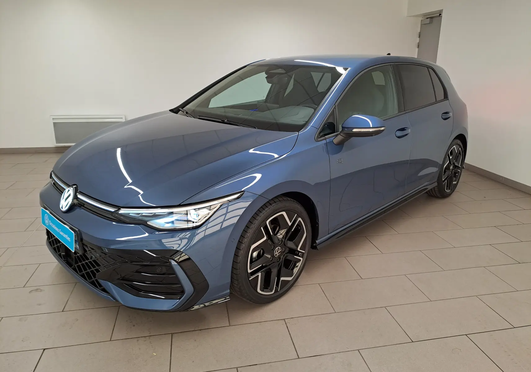 Volkswagen Golf 1.5 eTSI R-Line Bleu Anémone vue 3/4 avant droit en intérieur avec jantes distinctives.