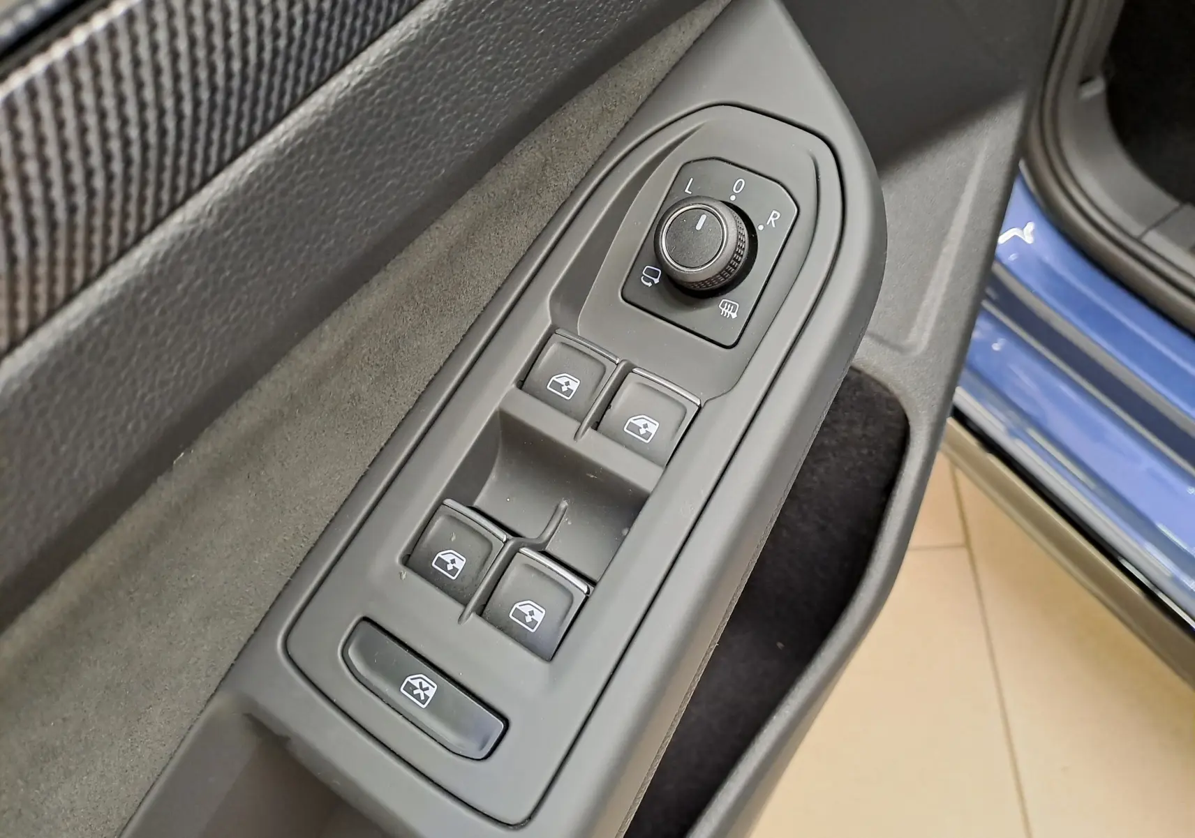 Gros plan sur les commandes de réglage des vitres et des rétroviseurs côté gauche d’une Volkswagen Golf Bleu Anémone 2025.