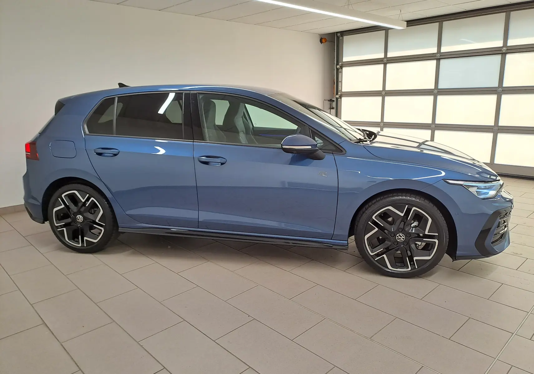 Volkswagen Golf 1.5 eTSI R-Line bleu anémone vue de profil côté gauche en intérieur lumineux.