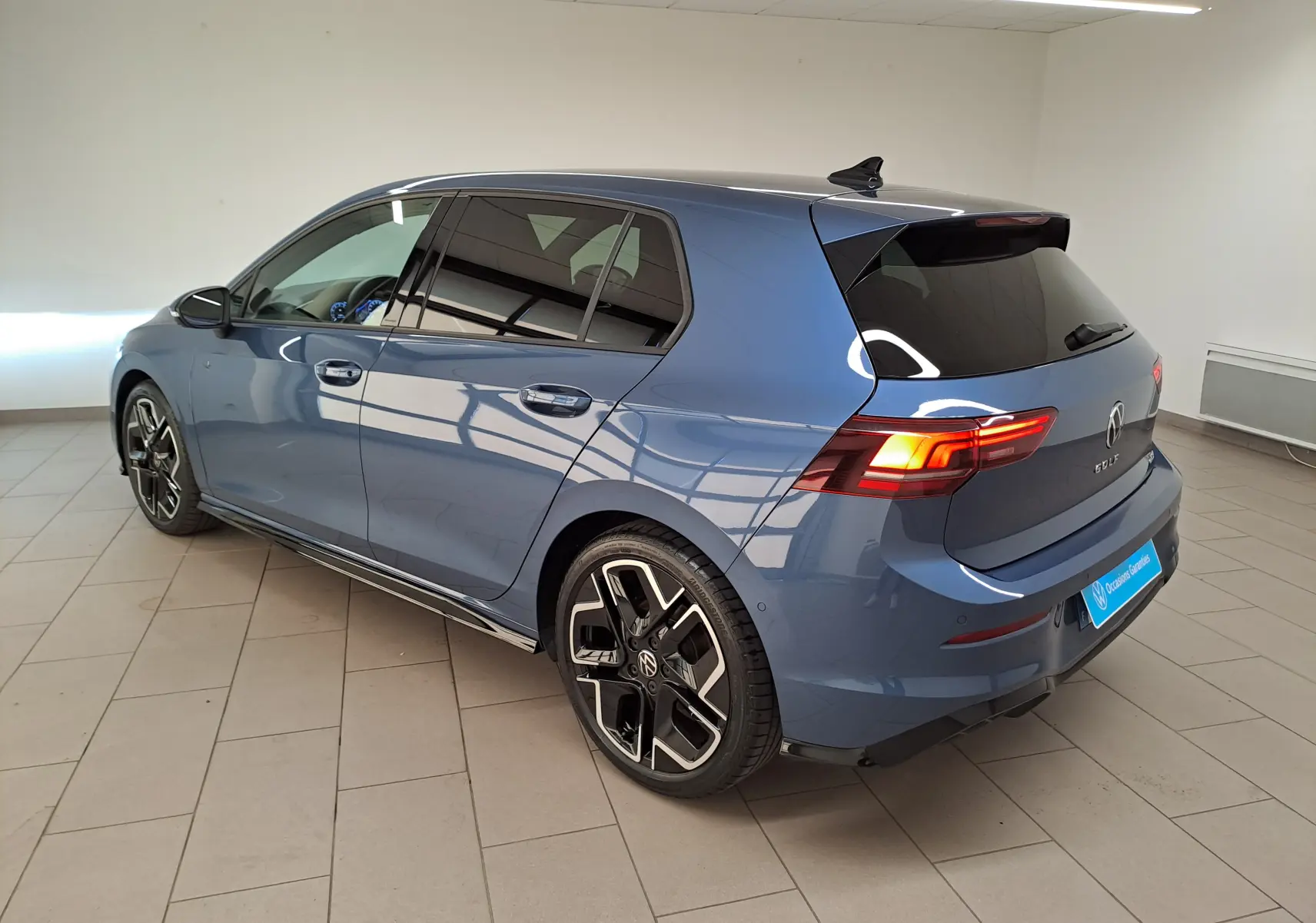 Volkswagen Golf 1.5 eTSI R-Line Bleu Anémone vue 3/4 arrière droit en intérieur avec jantes distinctives.
