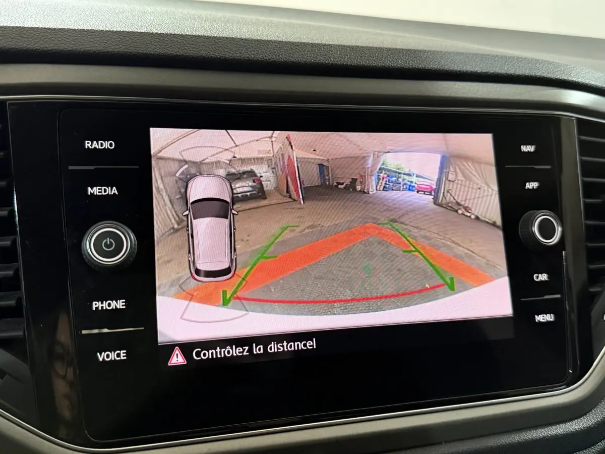 Écran tactile du tableau de bord affichant la caméra de recul du Volkswagen T-Roc blanc en intérieur de garage.