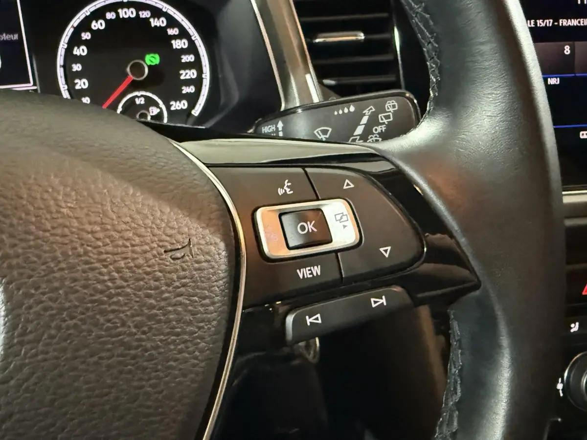 Gros plan sur le volant cuir noir du Volkswagen T-Roc 2020, avec commandes multifonctions et tableau de bord partiellement visible.