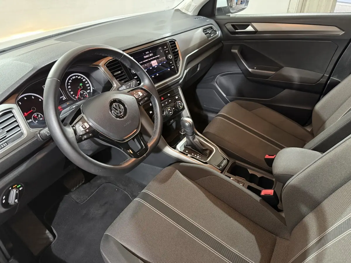 Intérieur du Volkswagen T-Roc 2020 vu côté conducteur, volant cuir noir et console centrale avec écran tactile.