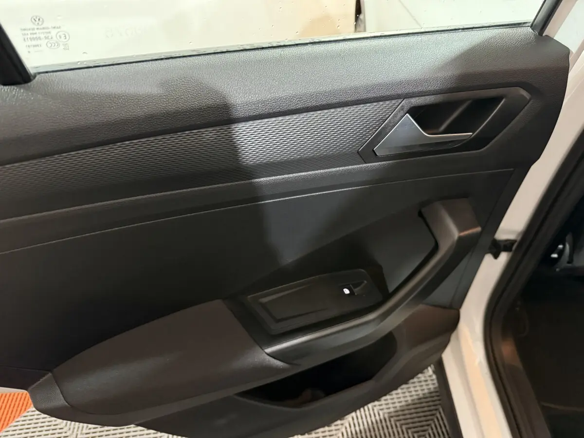 Intérieur côté gauche de la porte avant d'un Volkswagen T-Roc blanc, avec commande de lève-vitre et poignée noire.