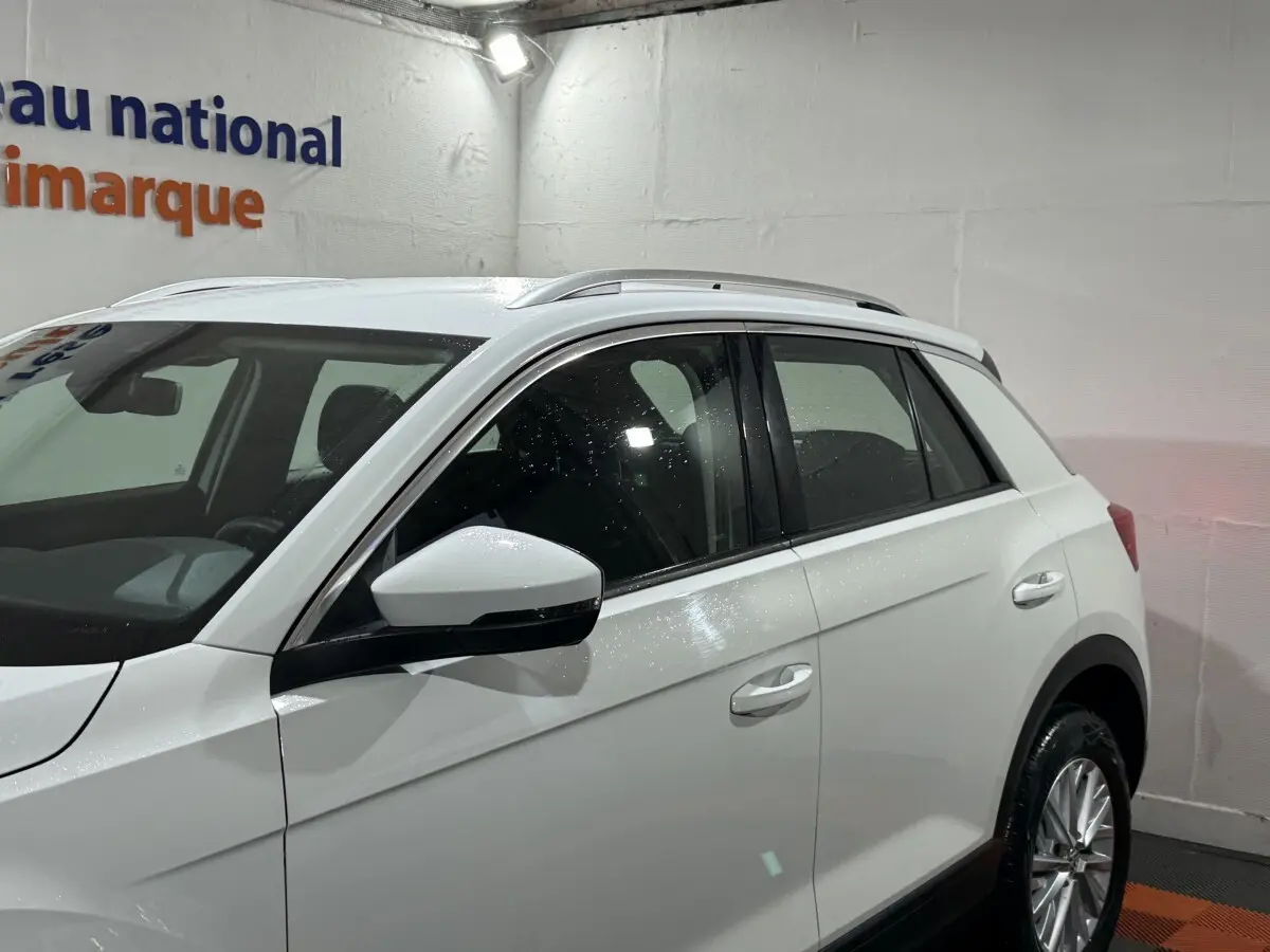 Vue côté gauche du Volkswagen T-Roc blanc 2020 en intérieur, mettant en valeur les rétroviseurs et les jantes alliage.