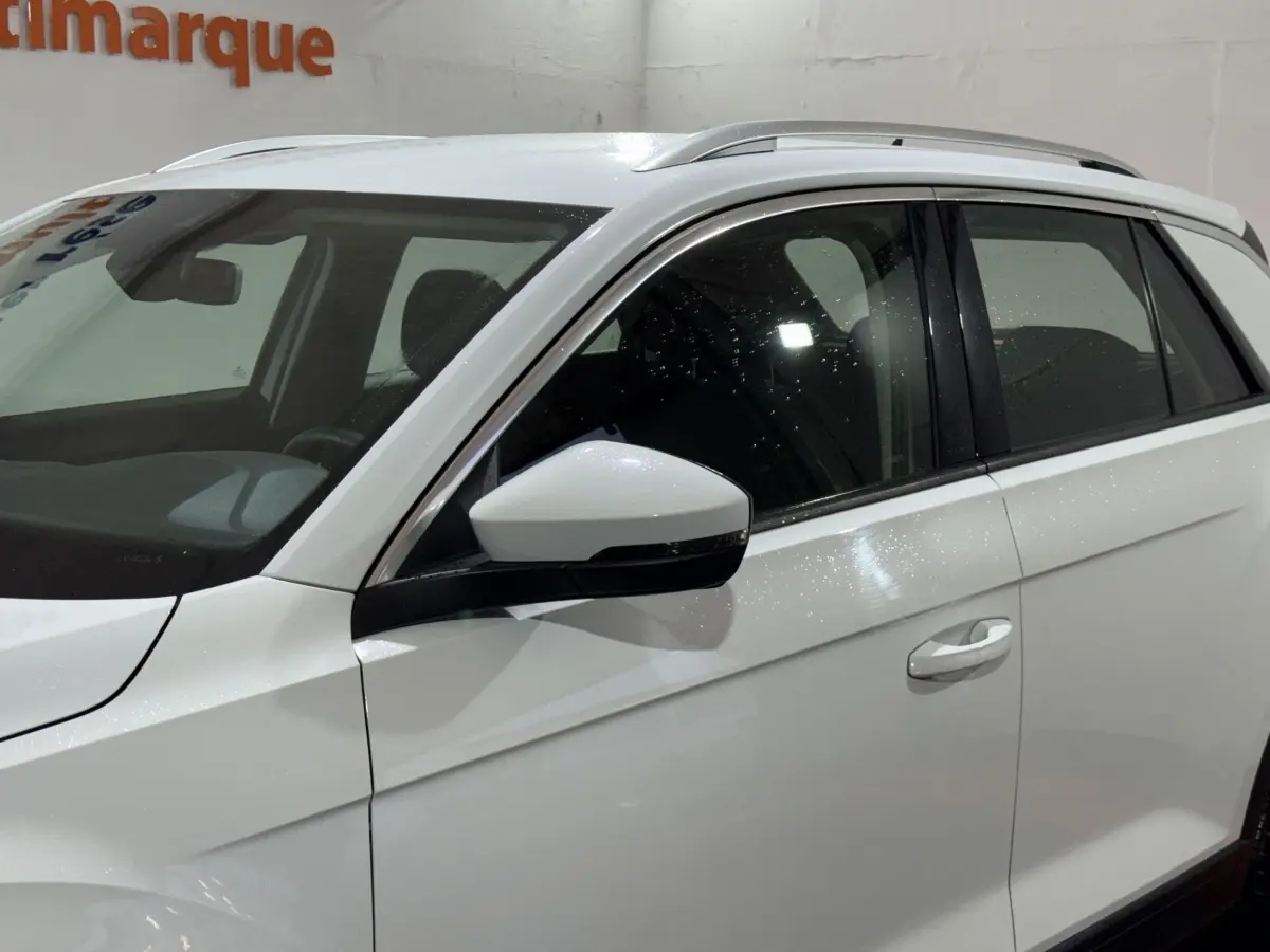 Vue latérale côté gauche d'un Volkswagen T-Roc blanc avec rétroviseurs électriques et rails de toit noirs.