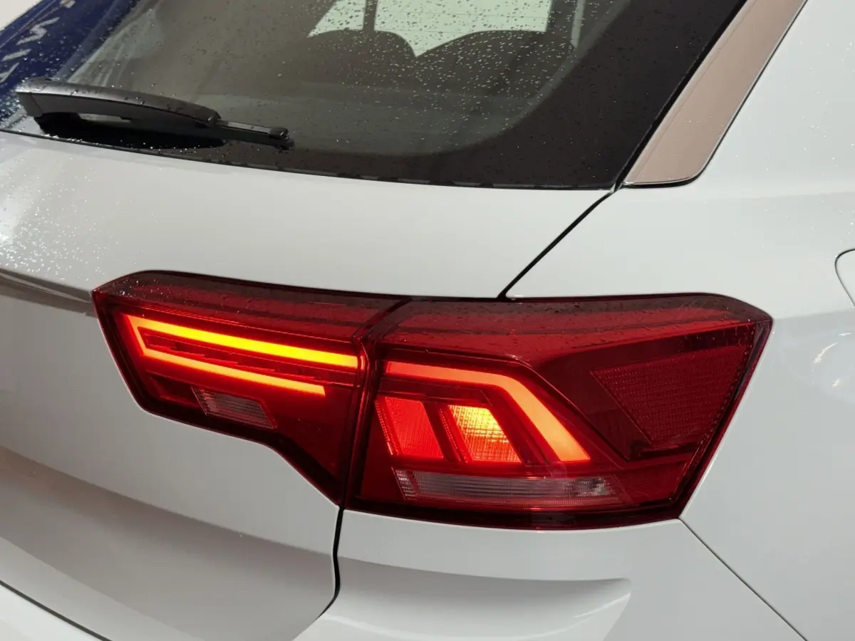Gros plan sur le feu arrière droit rouge allumé d'un Volkswagen T-Roc blanc, avec gouttes de pluie visibles sur la vitre arrière.