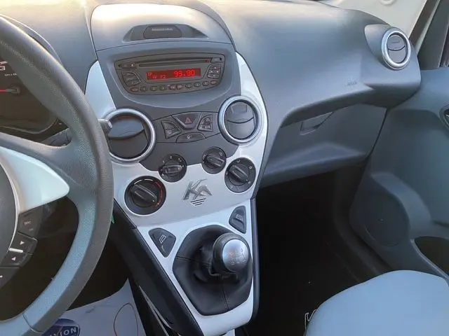 Vue intérieure du tableau de bord et console centrale blanche du Ford KA 1.2 69 TREND 2015 avec levier de vitesses manuel et commandes radio visibles.