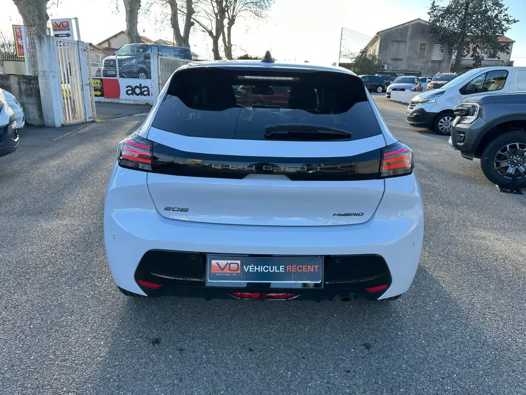 Vue arrière d'une Peugeot 208 Hybrid blanche de 2025 avec feux arrière LED et bande noire distinctive sur le hayon.