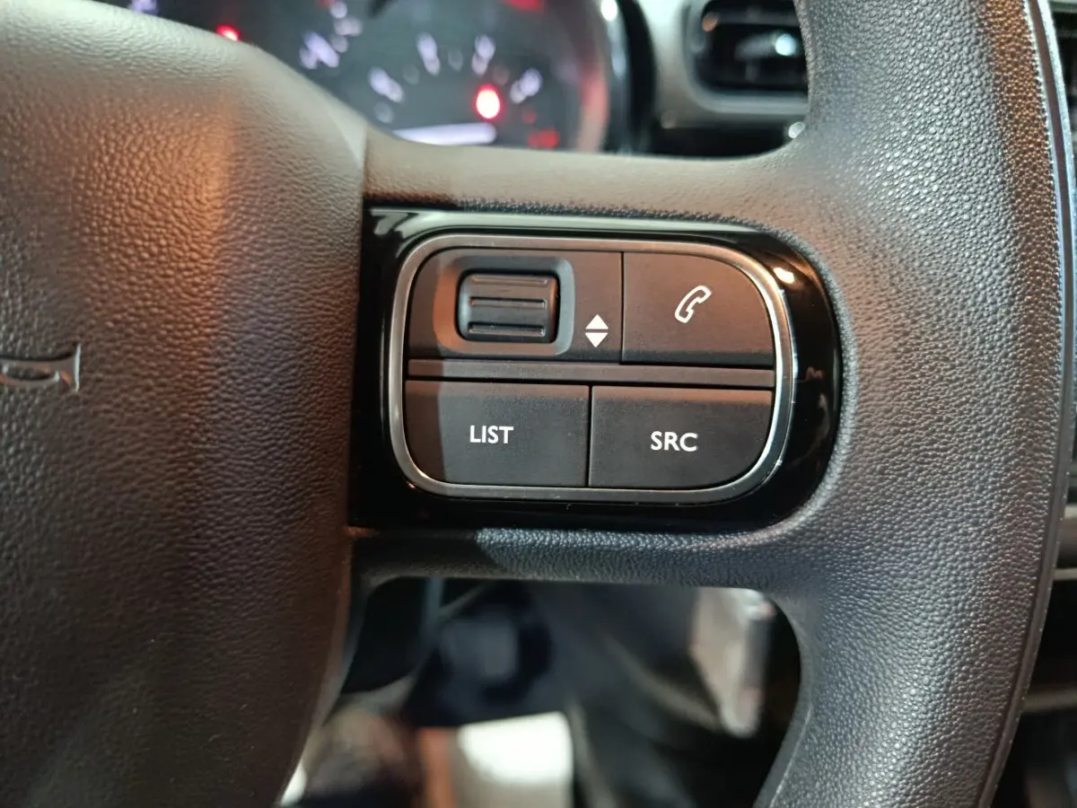 Gros plan sur les commandes gauche du volant noir de la Citroën C3 2024, boutons pour appels et listes multimédia.