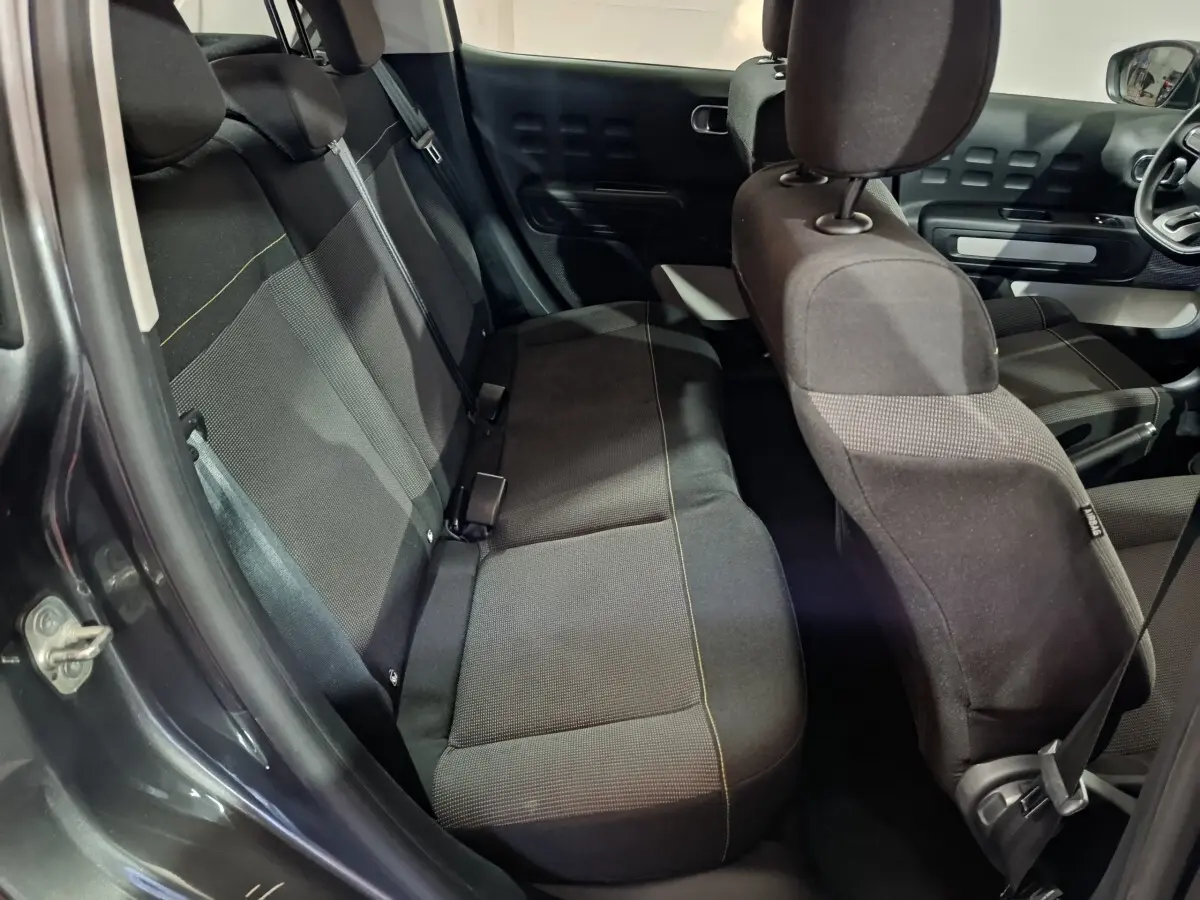 Vue intérieure côté arrière gauche d'une Citroën C3 gris foncé, montrant les sièges tissu et la banquette 3 places.