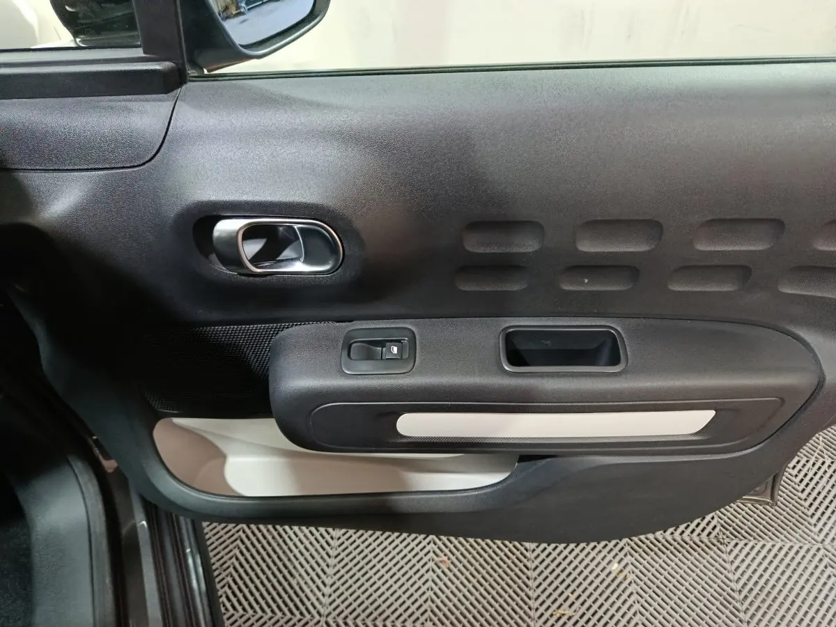 Vue rapprochée de la porte côté conducteur de la Citroën C3 gris foncé, avec poignée intérieure chromée et commandes électriques.