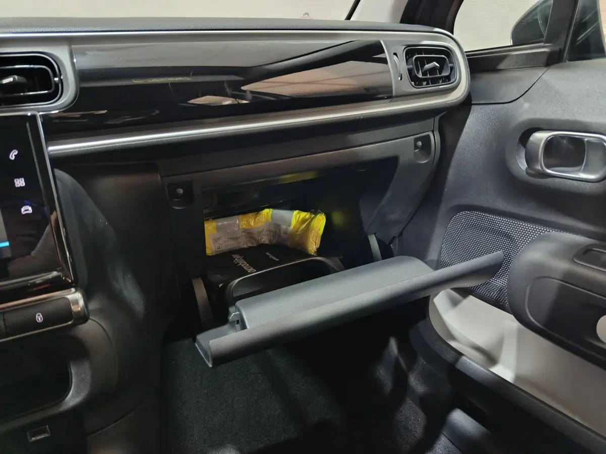 Intérieur de la Citroën C3 gris foncé, vue côté passager avec boîte à gants ouverte et tableau de bord moderne.