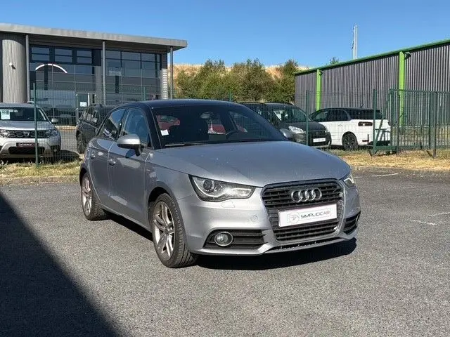 Audi A1 Sportback grise toit noir vue 3/4 avant droit sur parking avec calandre noire et jantes alliage.
