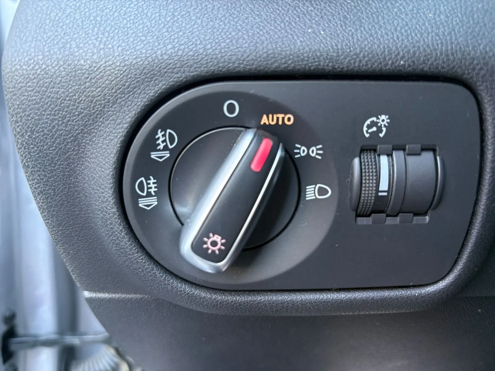 Gros plan sur le bouton de commande des phares avec réglage automatique dans une Audi A1 Sportback grise toit noir.