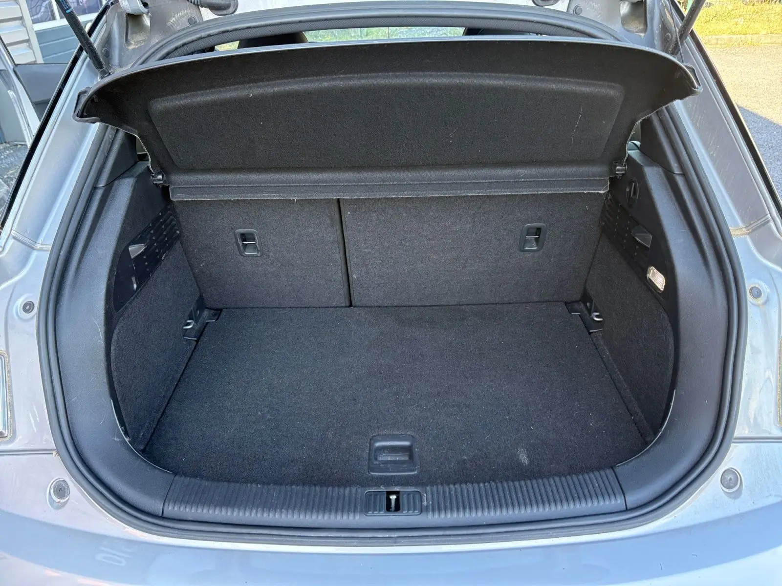 Coffre ouvert d’une Audi A1 Sportback grise, vue arrière, montrant l’espace de rangement vide et la moquette noire.