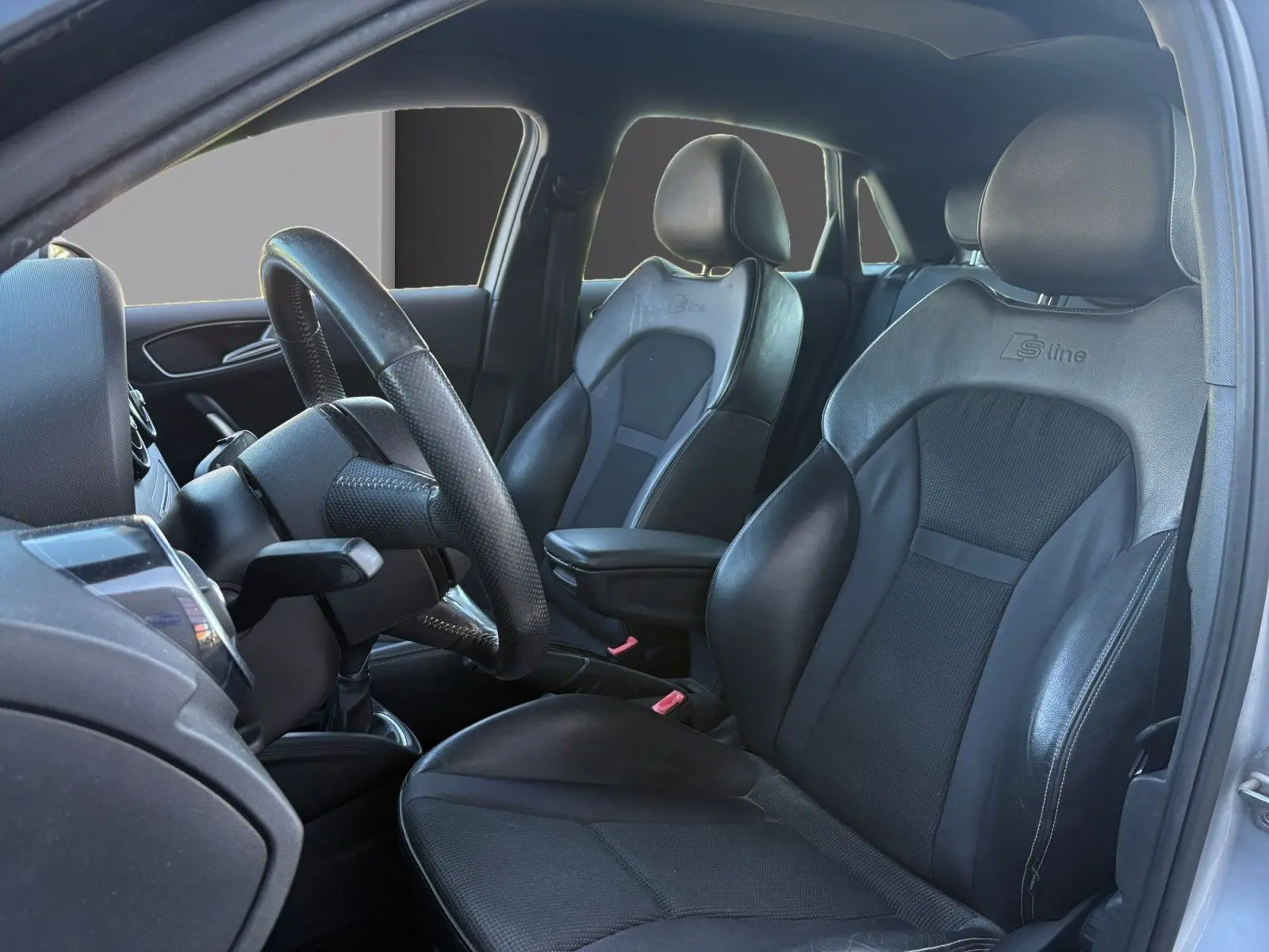 Vue intérieure côté conducteur de l'Audi A1 Sportback 1.4 TFSI S-Line 2014, sièges sport noirs avec logo S-Line visibles.