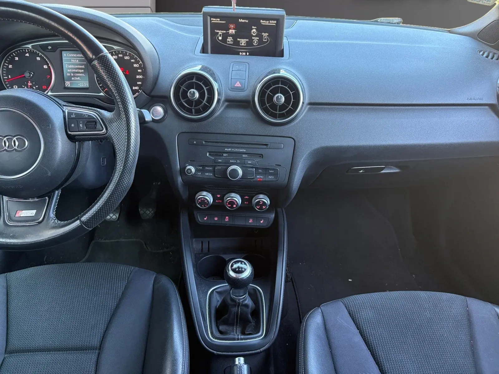 Vue intérieure de l'Audi A1 Sportback 1.4 TFSI 2014, tableau de bord noir avec volant sport et levier de vitesse manuel.