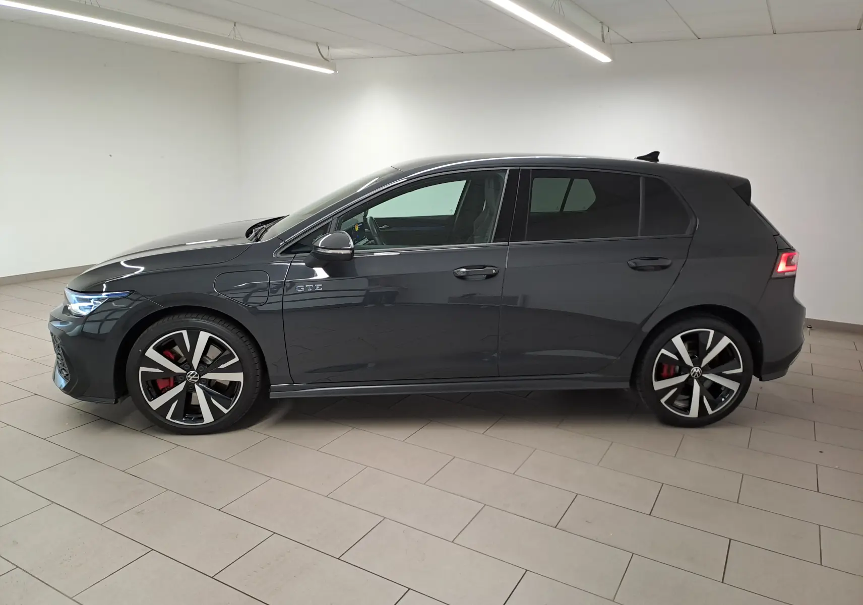 Vue de profil côté gauche d'une Volkswagen Golf 1.5 eHybrid 272 DSG6 GTE gris Urano avec jantes sport et feux arrière allumés.