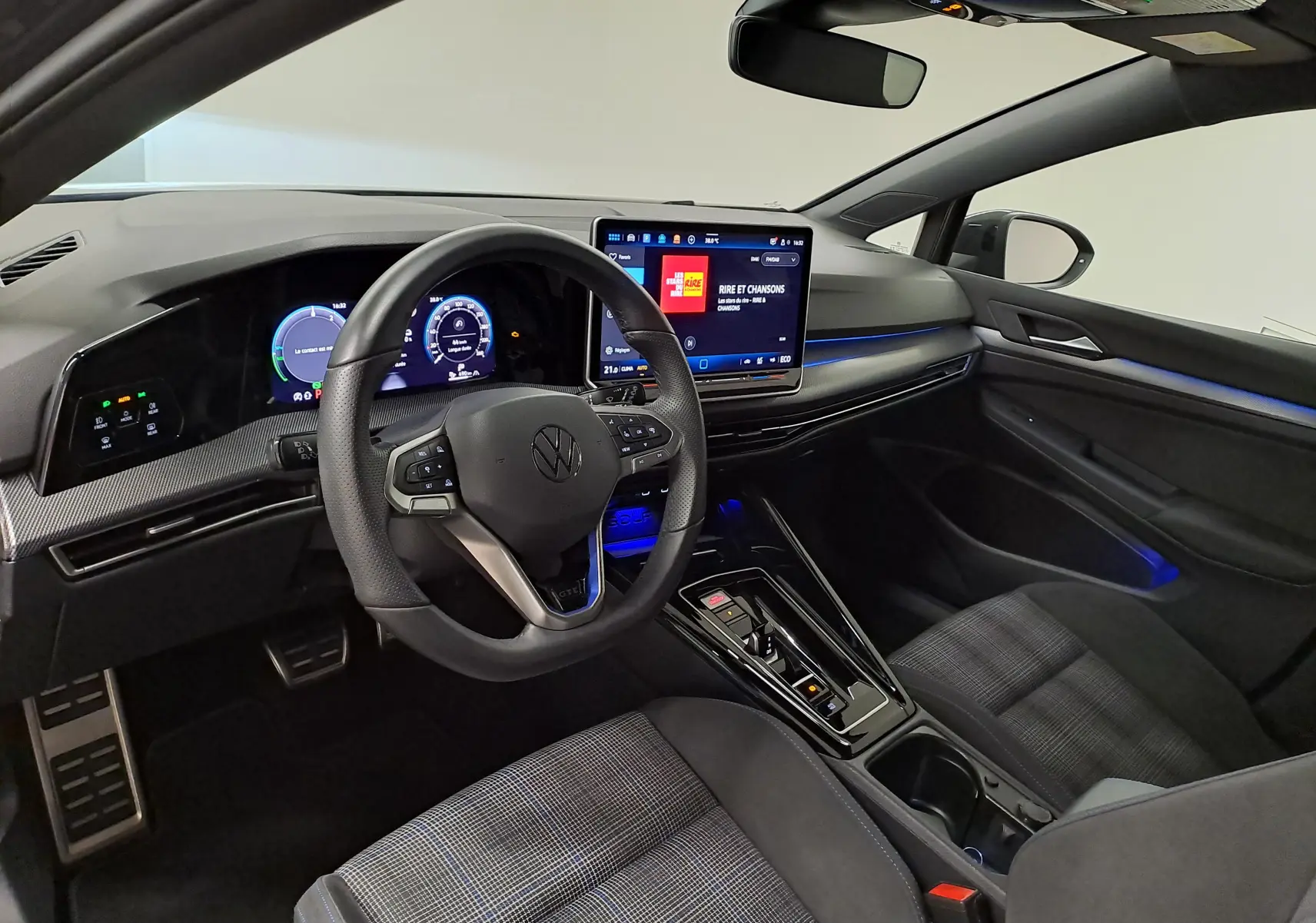 Vue intérieure côté conducteur de la Volkswagen Golf 1.5 eHybrid 2025 avec tableau de bord numérique et éclairage d'ambiance bleu.